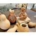 Unfinished dried gourds sitting next to finished gourd vases. They Feature butterflies and a sea turtle artwork drawn on the front.